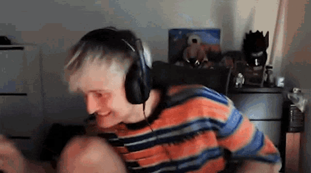 a young man wearing headphones and a striped shirt is dancing in a room .