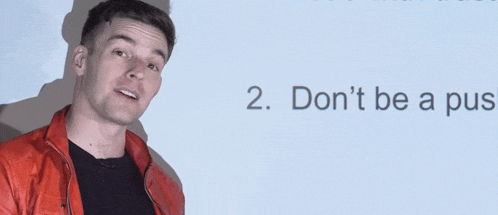 a man in a red jacket is standing in front of a white board that says " don 't be a pus "