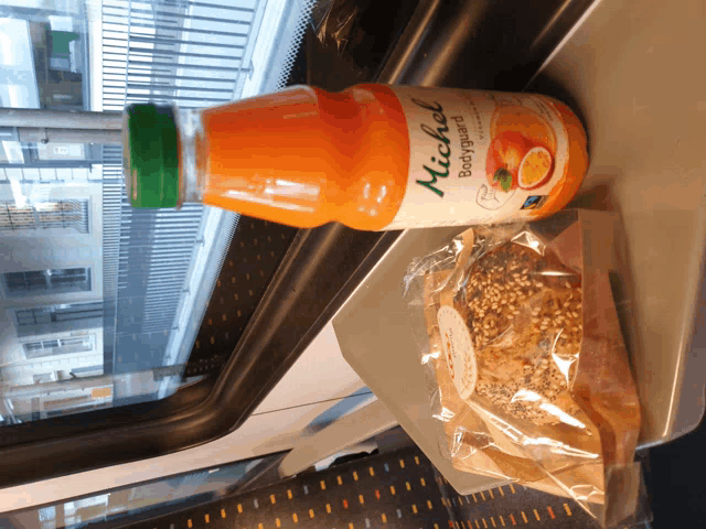 a bottle of michel orange juice sits next to a bag of food