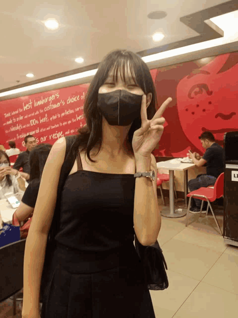 a woman wearing a black mask giving a peace sign in a restaurant