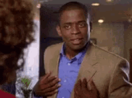 a man in a suit and a blue shirt is talking to a woman in a room .