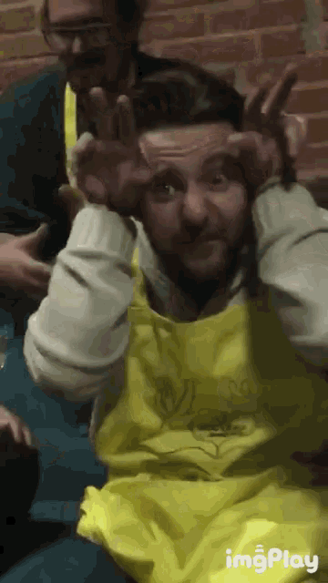 a man wearing a yellow apron is making a funny face with his hands on his head