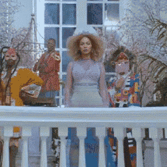 a woman with curly hair is standing on a balcony with a group of people behind her