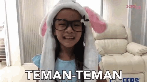 a little girl wearing glasses and a bunny hat says " teman-teman "