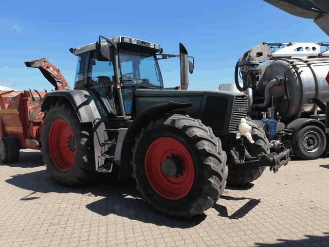 a green tractor with red tires is parked next to a silver tank