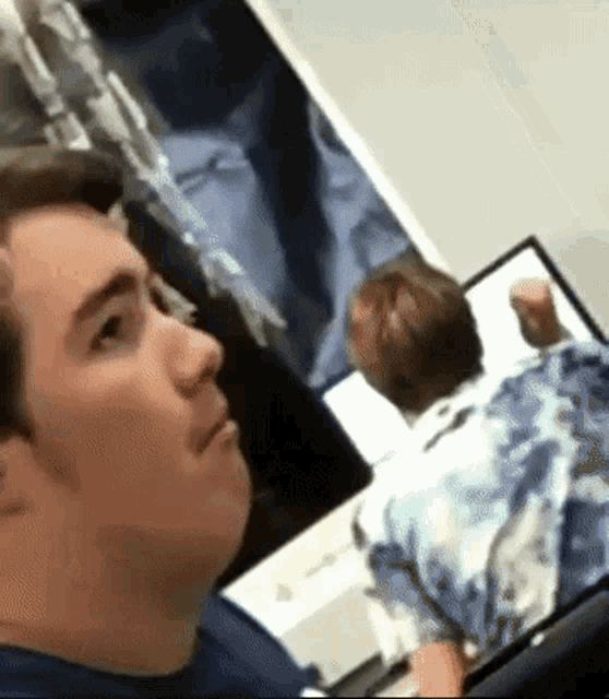 a man in a blue shirt is sitting in front of a laptop computer looking at something .