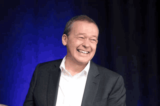 a man in a suit and white shirt is smiling in front of a blue background