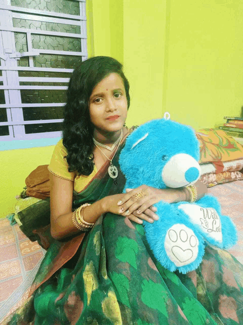 a woman sitting on a bed holding a blue teddy bear that says we love