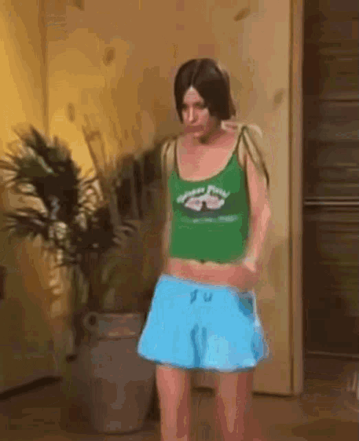 a woman in a green tank top and blue shorts is standing in a room