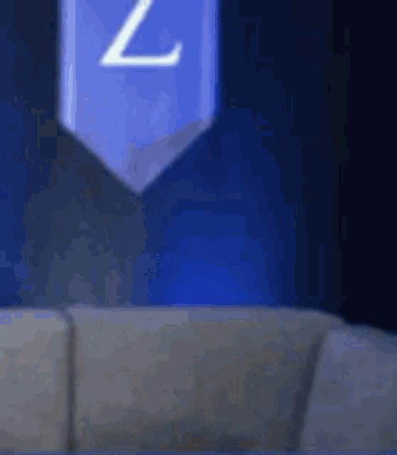 a blue flag with the letter z on it is hanging over a couch in a dark room .