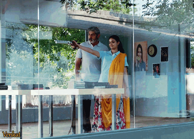 a man is pointing a gun at a woman in front of a glass wall with the word venkat on it