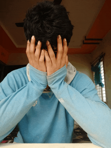 a man covering his face with his hands wearing a blue shirt with the word adidas on it