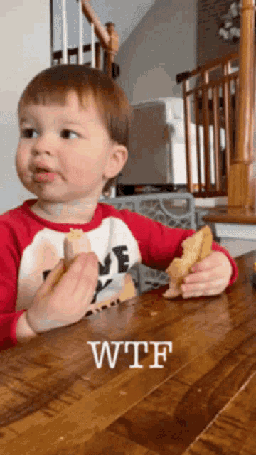 a little boy is sitting at a table eating a piece of food with the word wtf written on the bottom