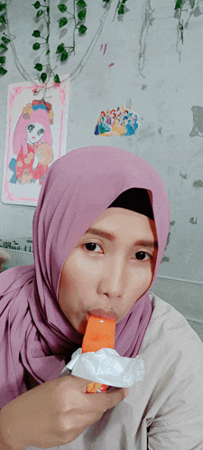 a woman wearing a purple hijab is eating an orange candy bar