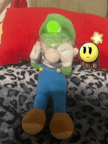 a stuffed mario with a green hat and blue overalls is sitting on a leopard print blanket