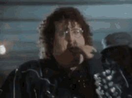 a man with curly hair and glasses is singing into a microphone in a dark room .