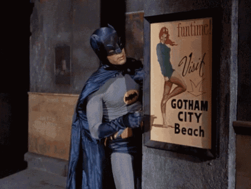 a man in a batman costume stands next to a sign that says gotham city beach