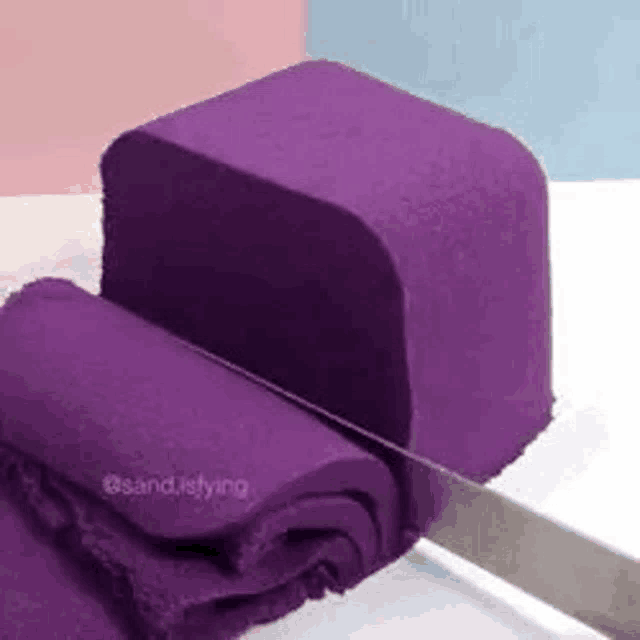 a block of purple sand is being cut in half with a knife .
