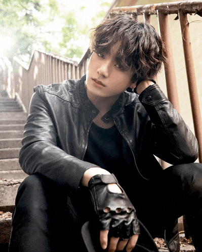 a young man wearing a leather jacket and gloves sits on some stairs