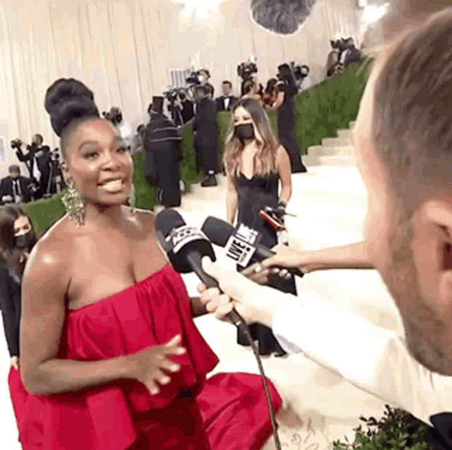 a woman in a red dress is being interviewed by a man with a microphone at a red carpet event .