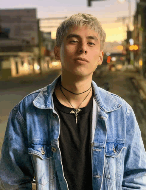 a young man wearing a choker and a denim jacket poses for a photo