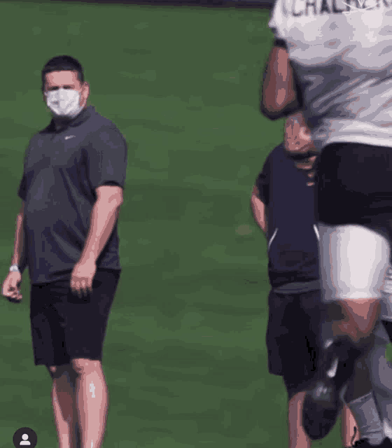 a man wearing a face mask watches a football player wearing a shirt that says chalmers