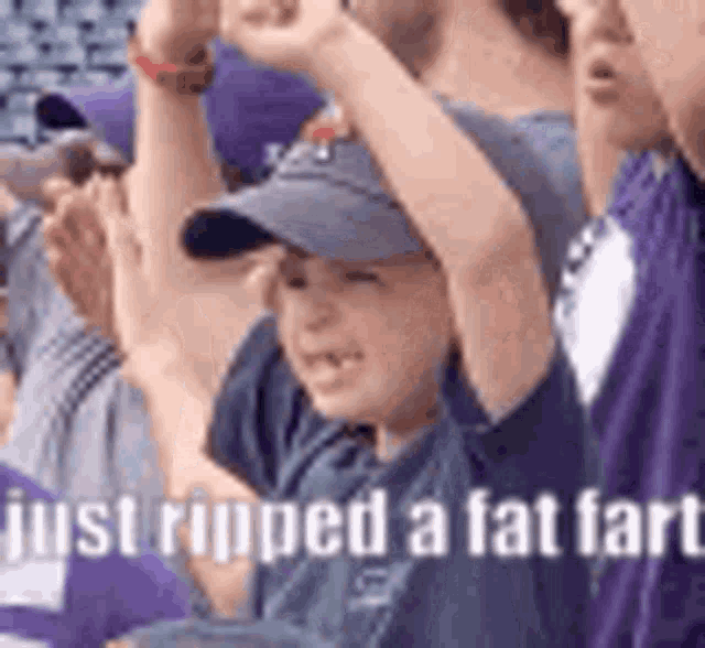 a group of people are sitting in a stadium with their arms in the air and a boy in a hat .