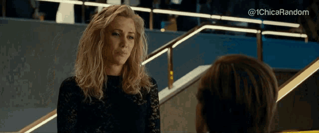 a woman in a black dress is talking to another woman in front of stairs