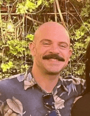 a bald man with a mustache is smiling for the camera while standing next to a woman .