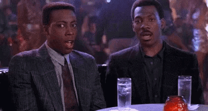 two men are sitting at a table with glasses of water in a bar .