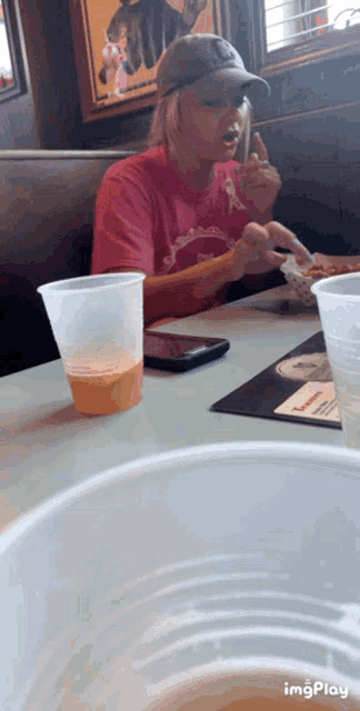 a woman in a red shirt is sitting at a table with a cup of orange juice in front of her