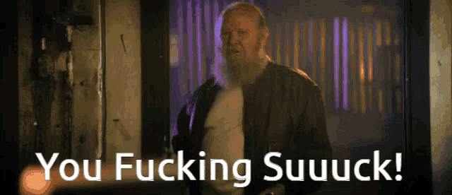 a man with a beard is standing in front of a sign that says " you fucking suuuck "