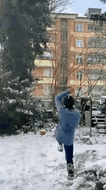 a woman is standing in the snow in front of a building and trees .