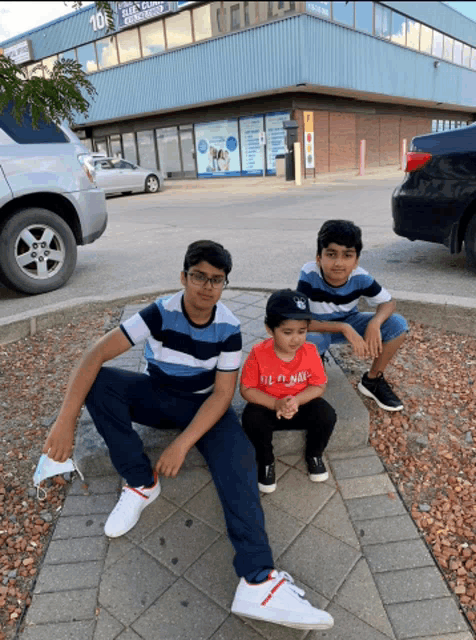 three young boys are sitting on a sidewalk in front of a building with a sign that says 10