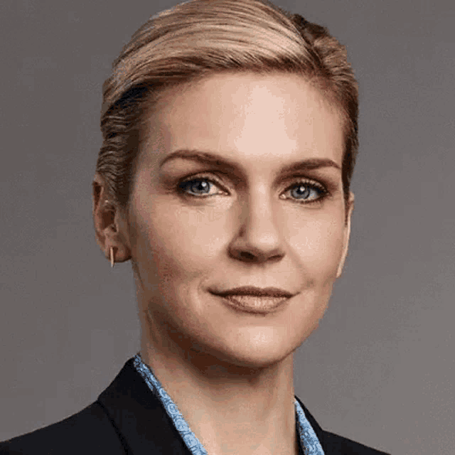 a close up of a woman 's face wearing a black jacket and a blue necklace .