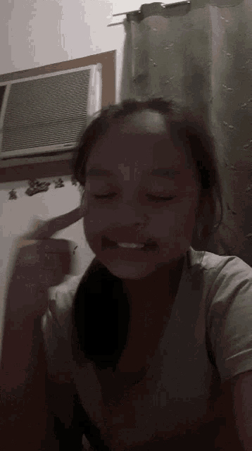 a girl is smiling with her eyes closed in front of a window