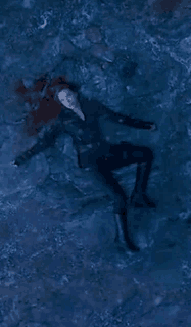 a woman in a black suit is laying on the ground in a body of water .