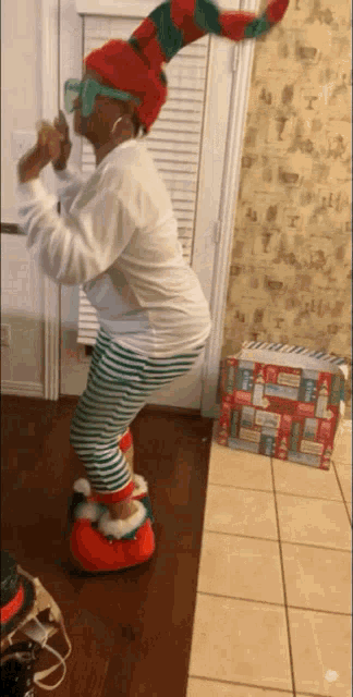 a woman wearing a santa hat and striped pants is standing in front of a christmas gift box