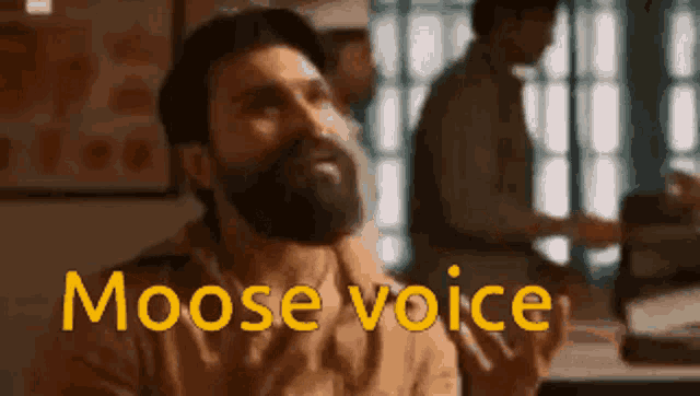 a man with a beard is sitting at a table with the words moose voice written on the screen .