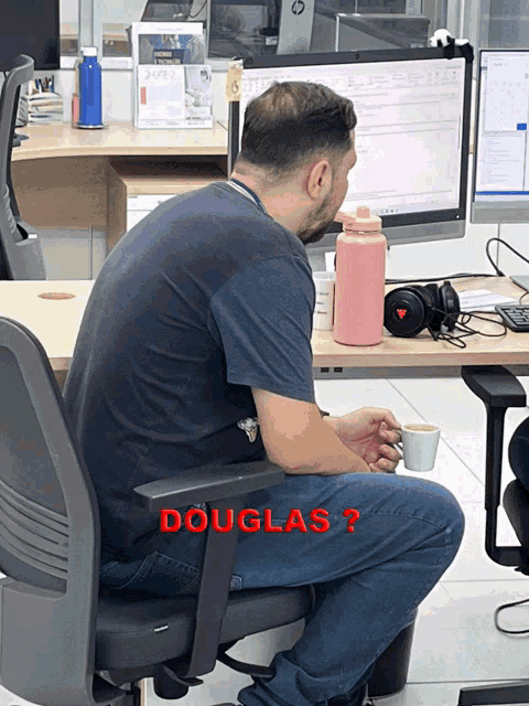 a man is sitting at a desk with a cup of coffee and the name douglas is on the bottom right