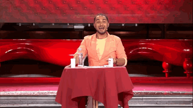 a man in an orange jacket stands at a table with a red tablecloth