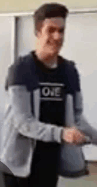 a man in a black shirt with the word one on it is standing in front of a whiteboard .