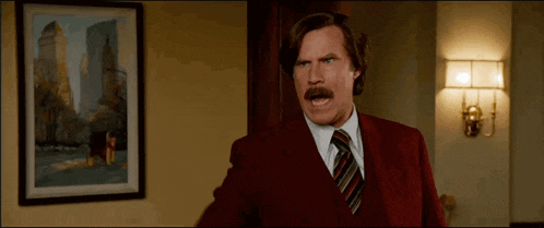 a man in a red suit and tie is standing in front of a picture .