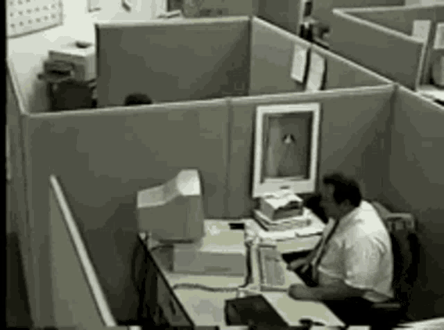 a man is sitting at a desk in an office cubicle with a computer