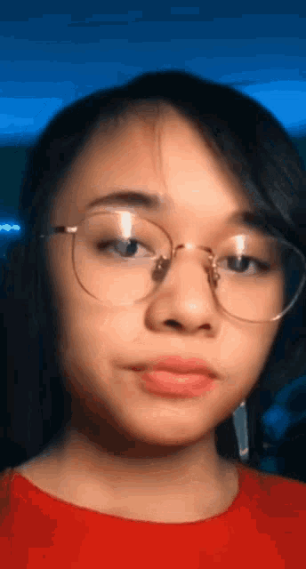 a young girl wearing glasses and a red shirt looks at the camera