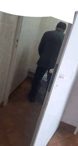 a man in a suit is urinating in a bathroom .