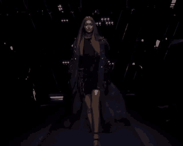 a woman in a black dress walks down a runway