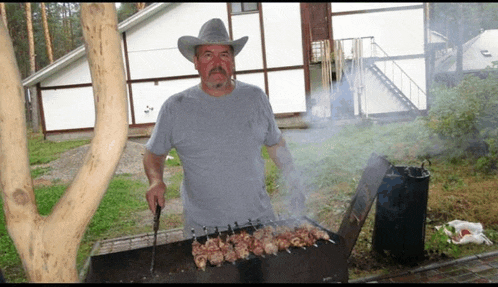 a man wearing a cowboy hat is grilling meat