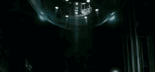 a man in a batman costume is flying through the air in a dark city at night .