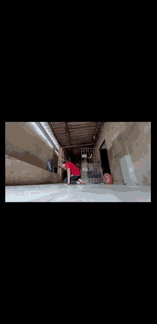 a person in a red shirt is kneeling on the floor in a room .
